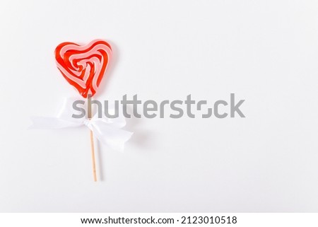 Heart-shaped lollipops on a stick with a white bow on a white background. Valentine's Day greeting card. Copy space. Flat lay, top view.