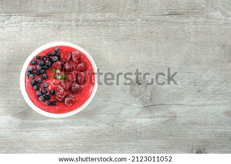 Top view white bowl with berry smoothie garnished with currants, raspberries and mint leaf on a gray wooden background. copy space for text