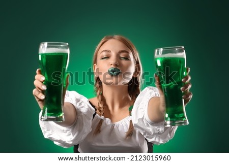 Beautiful Irish waitress with glasses of beer blowing kiss on green background. St. Patrick's Day celebration