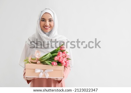 Muslim woman with tulips and gift box on light background. International Women's Day