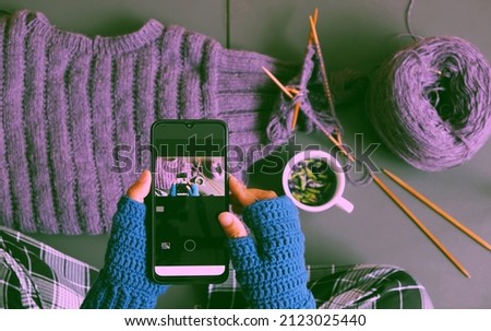 Top view woman hand wear blue mitten crochet, knit violet sweater for gift in wintertime, close hand press smartphone to take photo on dark tone