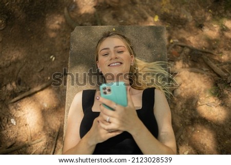 Young woman using a smartphone at day time lying down on a bench at a park. High quality photo. Mobile phone, technology, urban, nature  concept.