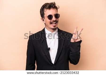 Young bodyguard caucasian man isolated on beige background joyful and carefree showing a peace symbol with fingers.