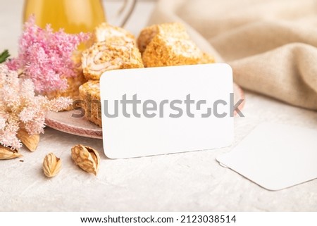 White business card with traditional turkish delight (rahat lokum) on white ceramic bowl on a gray concrete background. side view, close up.