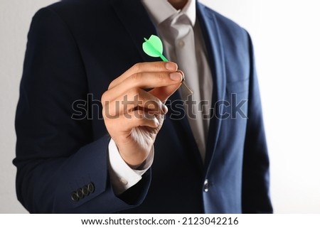 Man holding green dart on light background, closeup