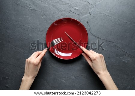 Woman with fork, knife and empty plate at black table, top view Royalty-Free Stock Photo #2123042273