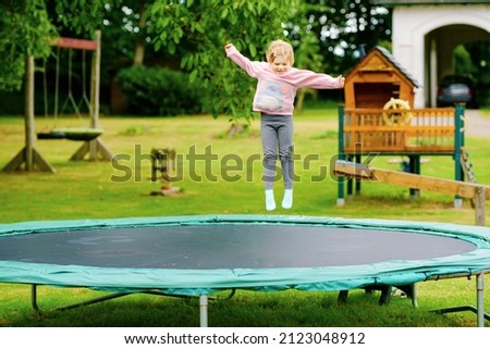 Little preschool girl jumping on trampoline. Happy funny toddler child having fun with outdoor activity in summer. Sports and exercises for children. Royalty-Free Stock Photo #2123048912