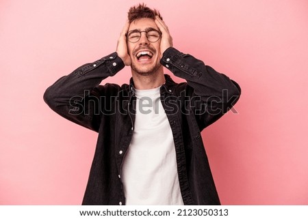 Young caucasian man isolated on pink background laughs joyfully keeping hands on head. Happiness concept.