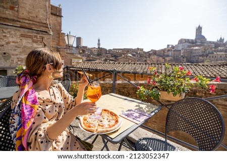 Young woman having lunch with pizza and wine at outdoor restaurant with beautiful view on the old town of Siena. Concept of italian cuisine and traveling Tuscany region of Italy Royalty-Free Stock Photo #2123052347