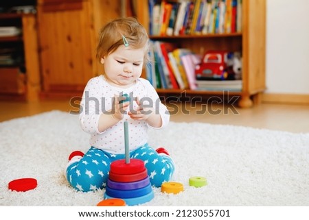 Adorable cute beautiful little baby girl playing with educational wooden toys at home or nursery. Toddler with colorful stack pyramid and music toy. Happy healthy child having fun with different toys.