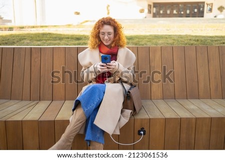 Young woman using her smartphone on a smart bench in a modern city Royalty-Free Stock Photo #2123061536
