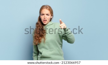 blonde pretty woman pointing at camera with an angry aggressive expression looking like a furious, crazy boss