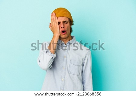 Young caucasian man with make up isolated on blue background  tired and very sleepy keeping hand on head.