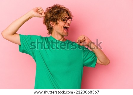 Young caucasian man with make up isolated on pink background celebrating a special day, jumps and raise arms with energy.