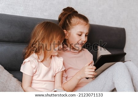 Two little girls sisters holding gadgets, spending time together. Happy children sitting in cozy bedroom and using technologies