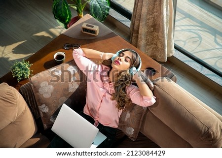 A young modern attractive and beautiful Asian Indian Latina female or woman is taking a break from work and absorbed in listening to music with eyes closed in an apartment or interior house setup.  Royalty-Free Stock Photo #2123084429