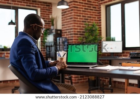 Entrepreneur using laptop with horizontal green screen to work on business project. Employee working with chroma key and isolated mockup template on computer display in startup office.