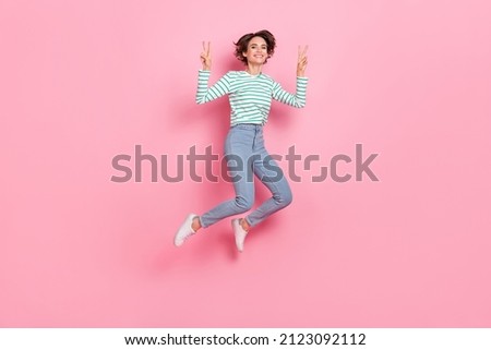 Full length body size view of attractive cheerful girly funny girl jumping showing v-sign isolated over pink pastel color background