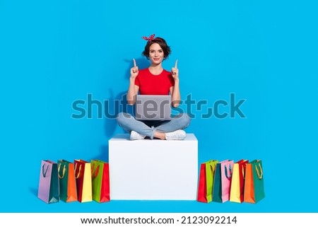 Full size photo of young girl indicate fingers empty space promo recommend select laptop shop isolated over blue color background