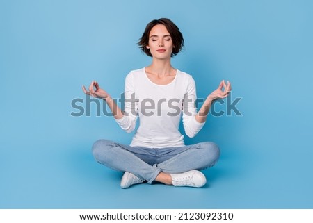 Photo of sweet adorable lady dressed white shirt smiling sitting legs crossed practicing yoga isolated blue color background