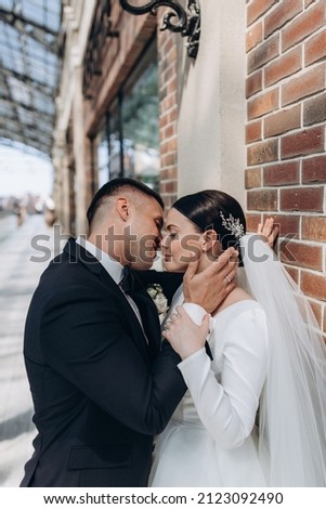 Facial portrait of a couple in love against a brick wall. The groom hugs the bride. The newlyweds are posing.