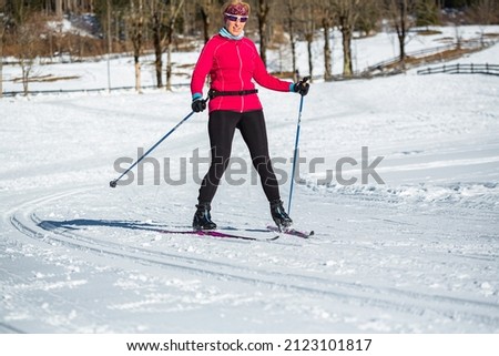 Middle aged woman, a recreational cross country skier, rides skis on the empty ski trail in the mountain foothill.