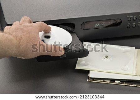 Hand of a man with a disc, an open tray of a CD player. Studio shot, close-up. Royalty-Free Stock Photo #2123103344