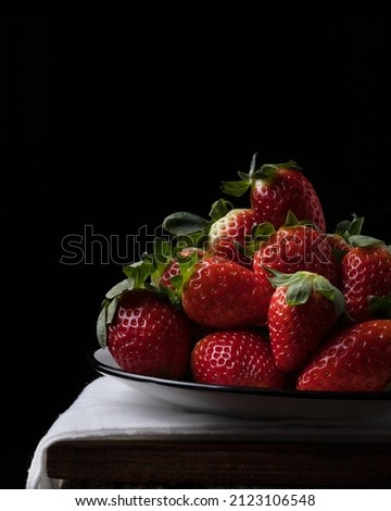 A photo of red strawberries on a black plate and a black background