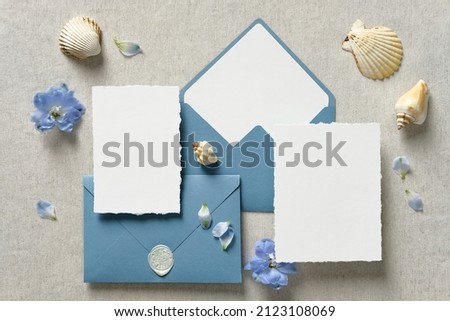 Nautical wedding invitation cards and blue envelopes with seashell and flowers on beige background. Sea wedding stationery set. 