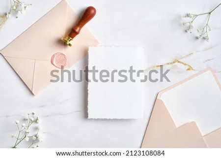 Wedding stationery set on marble desk top view. Blank paper card mockup, pastel pink envelopes with wax seal stamp, gypsophila flowers. Royalty-Free Stock Photo #2123108084
