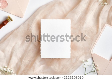 White paper card mockup with pink wedding envelopes, wax seal stamp, spring flowers on beige cloth. Wedding invitation template.