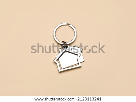 Silver house shaped keychain with keyring on beige background