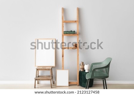 Blank poster on step ladder with decor near light wall