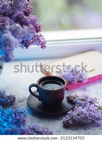 Spring still life with a cup of coffee and bouquets of lilacs. Colored light.