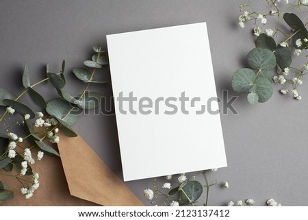 Wedding invitation or greeting card mockup with envelope, eucalyptus and gypsophila plants decorations, top view