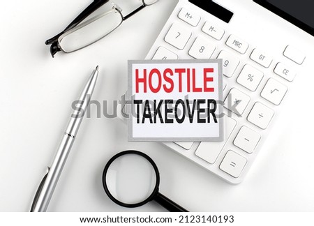 HOSTILE TAKEOVER text on sticker with calculator, glasses and magnifier Royalty-Free Stock Photo #2123140193