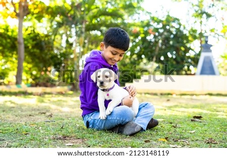 focus on dog, Young Indian Kid playing by holding puppy dog at park - concpet companion, friendship, childhood and recreation Royalty-Free Stock Photo #2123148119