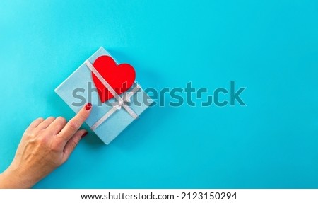 Woman hand points finger gift decorated with silver ribbon, blue background, copy space. Flat lay, hand and present box, top view. Valentine or love, spring holidays, Christmas and birthday concept.