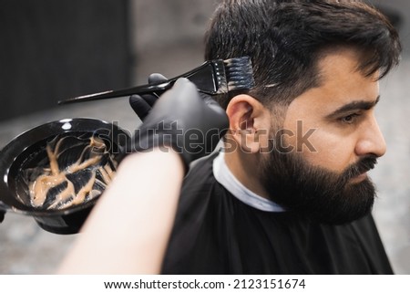 Professional barber dying male client hair in barbershop. Hairdresser applies dye to the client's hair with a brush Royalty-Free Stock Photo #2123151674