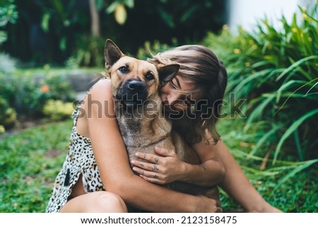 Young woman hugging her dog in yard of resort hotel. Tourism, vacation and weekend. Owner and pet relationship and friendship. Attractive caucasian girl wear dress. Idyllic and tranquil lifestyle Royalty-Free Stock Photo #2123158475
