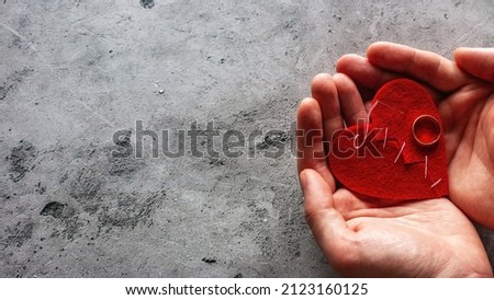 holds in the palms a broken heart sewn with threads and a wedding ring the concept of divorce with a place for text on a gray background