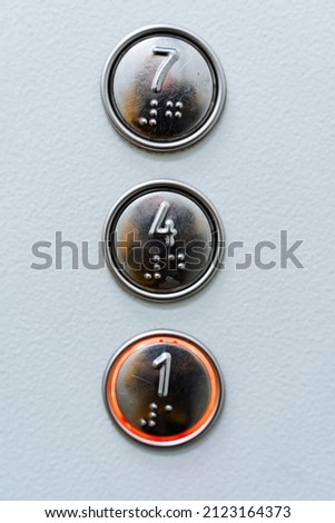 An approximate shot of three elevator buttons. Seven, four, one. Burning elevator call button. Font for the blind on the elevator panel. High quality photo