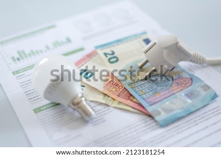  a white electric cap, a light bulb and euro banknotes on an electric bill. Increase in the cost of electricity . Payment of electricity bills. Increasing the concept of electricity prices. Royalty-Free Stock Photo #2123181254