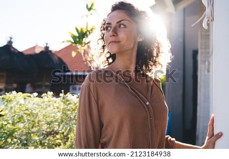 Contemplative female with curly hair thoughtful looking away thinking about weekend pastime during sunny vacations, pensive hipster girl dressed in casual wear spanding daytime outdoors Royalty-Free Stock Photo #2123184938