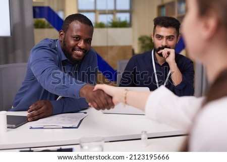 Happy young African-American businessman shaking hand of female expert in lab coat over desks with medical or financial papers Royalty-Free Stock Photo #2123195666