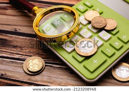Real currency - BRL. Brazilian coins on a calculator and wooden table with a magnifying glass in the image composition. Concepts of Brazilian economy, inflation and debts.
 Royalty-Free Stock Photo #2123208968
