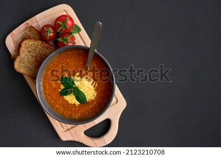 A plate of tomato soup on a black background. Tomatoes, greens, wooden board. View from above. Place for text