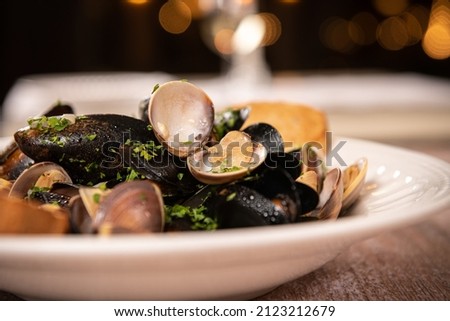 Food photography. Plate with mussels in wine sauce, close up view against a wooden table. Delicious seafood.