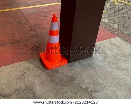 the unused traffic cone is in the parking lot next to the building support