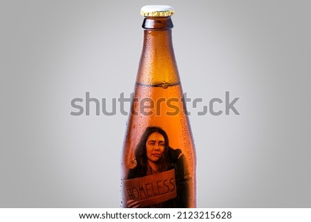 Close-up of a wet bottle of dark beer with a picture of homeless person inside. Gray background. The concept of alcoholism and social problems.